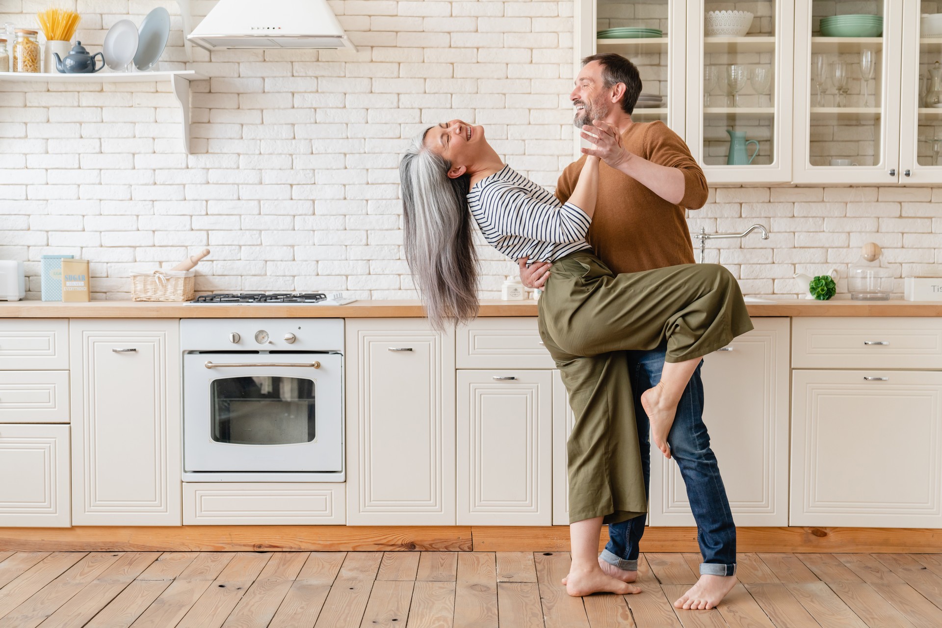 Mature middle-aged family couple husband and wife dancing in the kitchen, celebrating date, anniversary. Love and relationship. Social distansing, lockdown concept